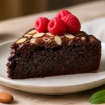 Part de gâteau pour diabétique au chocolat noir, garnie de framboises fraîches et d'amandes effilées sur table boisée.