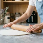 Pâtissière étalant une pâte à sucre blanche lisse sur un plan de travail en marbre pour une recette maison.