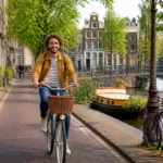 Cycliste à Amsterdam le long des canaux, entre maisons historiques et pont pittoresque, idéal pour visiter Amsterdam en 3 jours