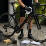 Entretien vélo carbone : cycliste ganté essuyant délicatement le cadre avec un chiffon doux après le nettoyage.
